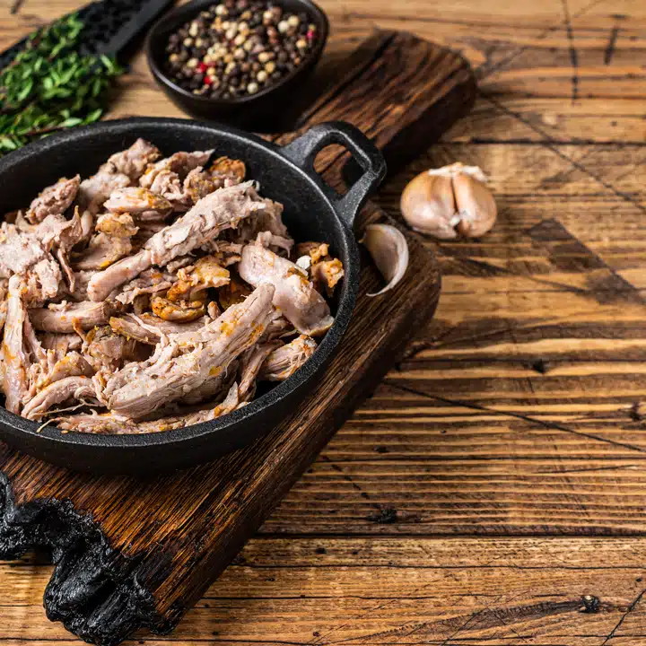 Slow shredded puilled pork meat in a pan with butcher knife. wooden background. Top view. Copy space.