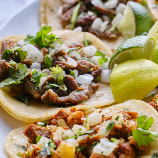 An image showing Al Pastor tacos with diced onions, chopped cilantro, and lime wedges.