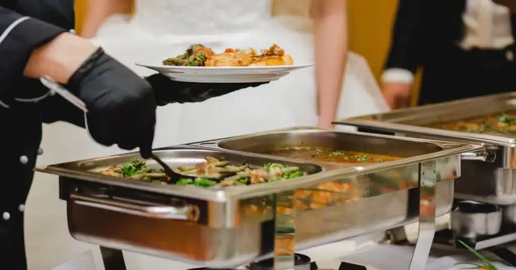 An image showing a catering setup with diverse food options and a chef serving guests at an event.